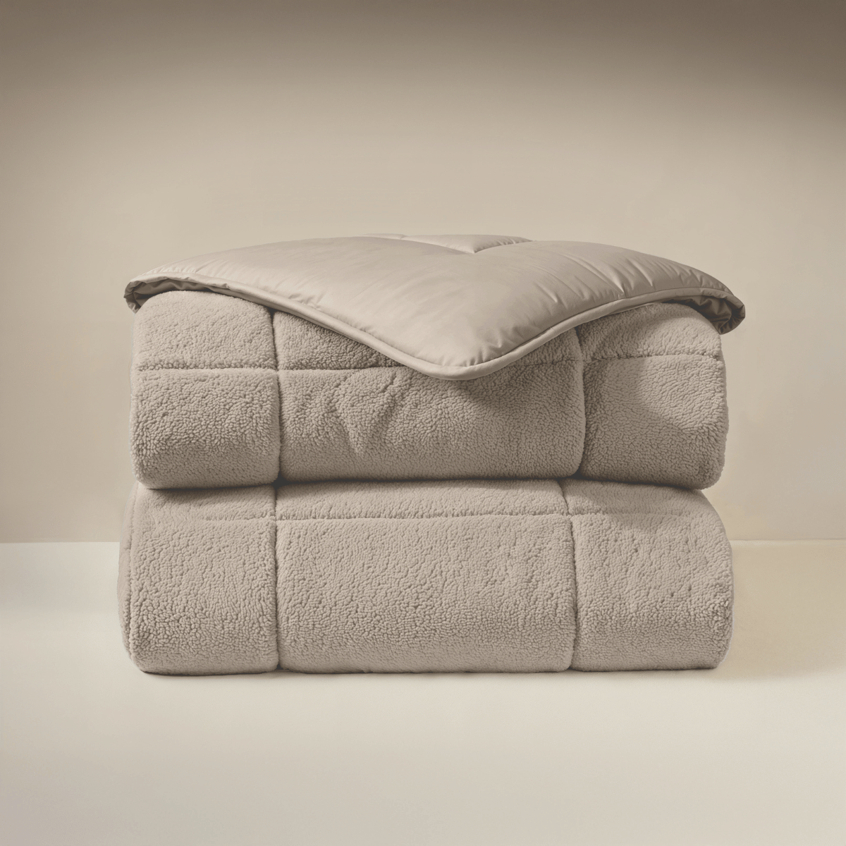 Het Zelesta Teddybed - Taupe, met een zachte teddystoftextuur, is netjes gevouwen en gestapeld tegen een neutrale achtergrond.