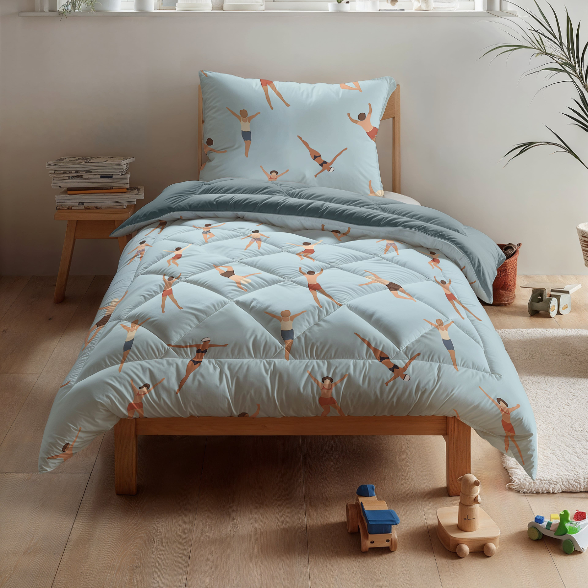 Een opgeruimde kamer met een kinderbed met het Zelesta Kiddybed Katoen - Swimmers beddengoed in lichtblauw, houten speelgoed, planten en een praktisch wasbaar dekbed op een houten vloer.