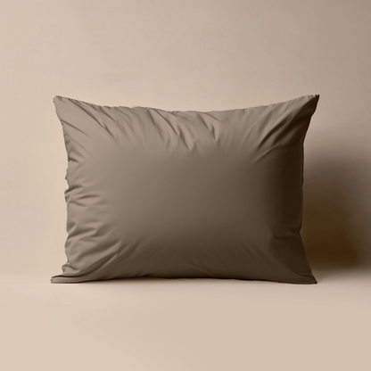 Een Zelesta Premiumbed Kussensloop in taupe, gemaakt van perkal katoen, staat rechtop tegen een lichtbeige achtergrond.