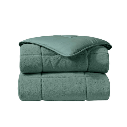 Het Zelesta Teddybed - Groen is een gevouwen, lichtgroen gewatteerd dekbed met een pluche textuur en gladde teddystof toplaag, weergegeven op een witte achtergrond.