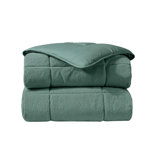 Het Zelesta Teddybed - Groen is een gevouwen, lichtgroen gewatteerd dekbed met een pluche textuur en gladde teddystof toplaag, weergegeven op een witte achtergrond.