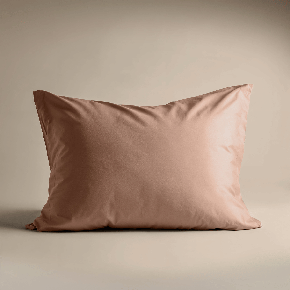 Een enkel lichtbruin kussen met een glad, zijdezacht oppervlak rust rechtop tegen een beige achtergrond - perfect om te combineren met de Zelesta Satinbed Kussensloop Set van 2 - Timeless Terra voor een luxe bedstijl.