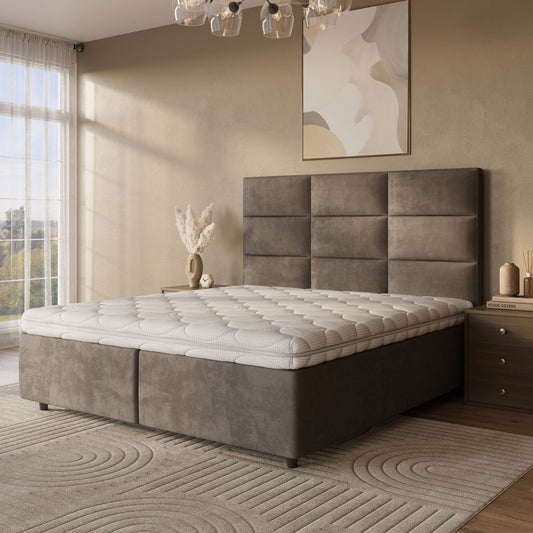 Een moderne slaapkamer met een groot gestoffeerd bed met de Topdekmatras - Latex Schuim Tencel Tijk voor drukverlagende ondersteuning, een geometrisch hoofdbord, neutraal beddengoed, een nachtkastje met boeken en decor, abstracte kunst en een groot raam met transparante gordijnen.