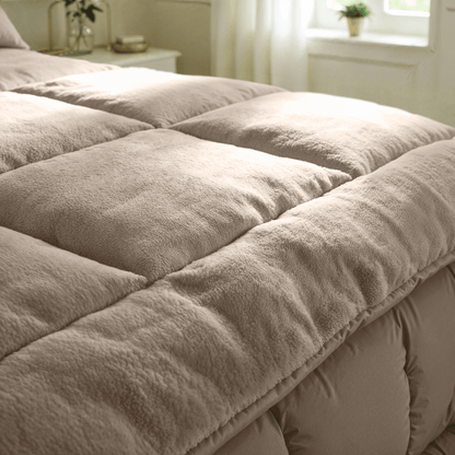 Close-up van een netjes opgemaakt bed met het Zelesta Teddybed - Taupe, een dik, pluche dekbed in zachte verlichting voor ultiem comfort.