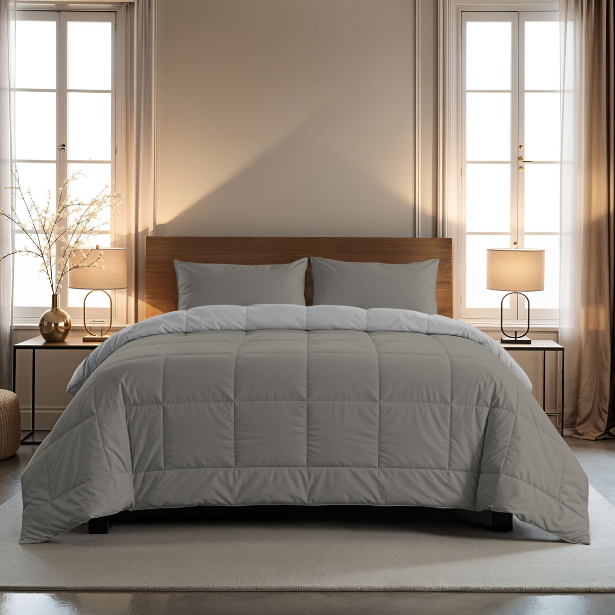 Een keurig opgemaakt bed met het Zelesta Comfort Duo Dekbed in Grijs & Zacht grijs en twee kussens, gecentreerd tussen ramen met beige gordijnen, geflankeerd door nachtkastjes en lampen.