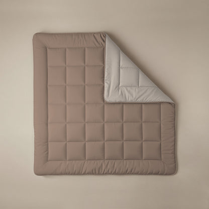 Het Zelesta Comfort Duo Dekbed - Terra & Zand is een bruine gewatteerde deken met een rasterpatroon, geïnspireerd op klassieke dekbedden. De deken is gedeeltelijk opgevouwen zodat de lichtgrijze onderkant zichtbaar wordt, en plat neergelegd voor een look het hele seizoen door.