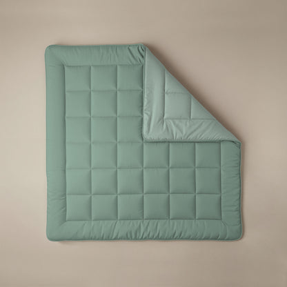 Het Zelesta Comfort Duo Dekbed in mintgroen & lichtgroen ligt plat op een beige ondergrond, met één hoek omgevouwen om de onderkant te laten zien - ideaal als gewatteerde deken voor alle seizoenen.