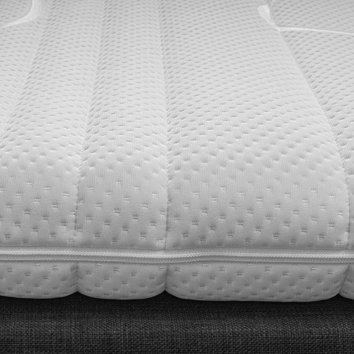 Close-up van de Silver Line Topper - Hybrid Koudschuim, een witte, gestructureerde matras met doorgestikt patroon en zichtbare stiksels, rustend op een bedbodem van donkere stof, gemaakt van natuurlijke materialen voor een gezonde slaapomgeving.