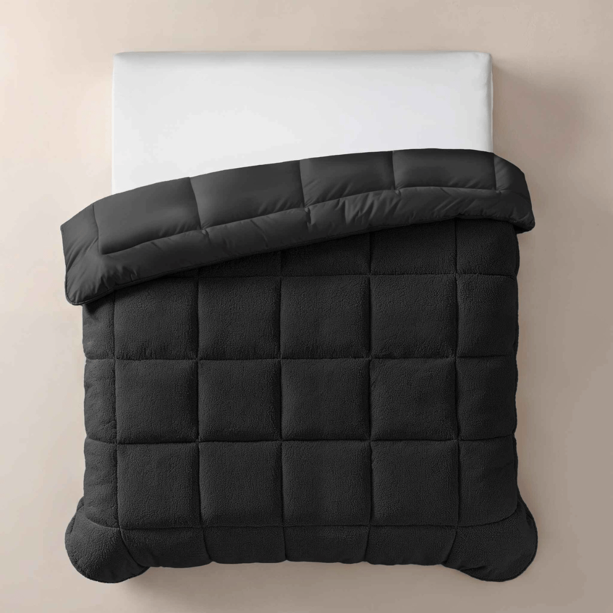 Op een netjes opgemaakt bed ligt het Zelesta Teddybed - Antraciet, een doorgestikt antraciet dekbed dat aan de bovenkant is omgeslagen met een wit kussen voor een knusse touch.