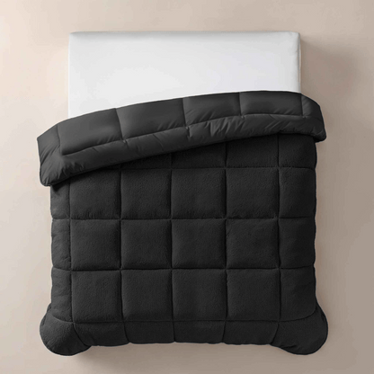 Op een netjes opgemaakt bed ligt het Zelesta Teddybed - Antraciet, een doorgestikt antraciet dekbed dat aan de bovenkant is omgeslagen met een wit kussen voor een knusse touch.