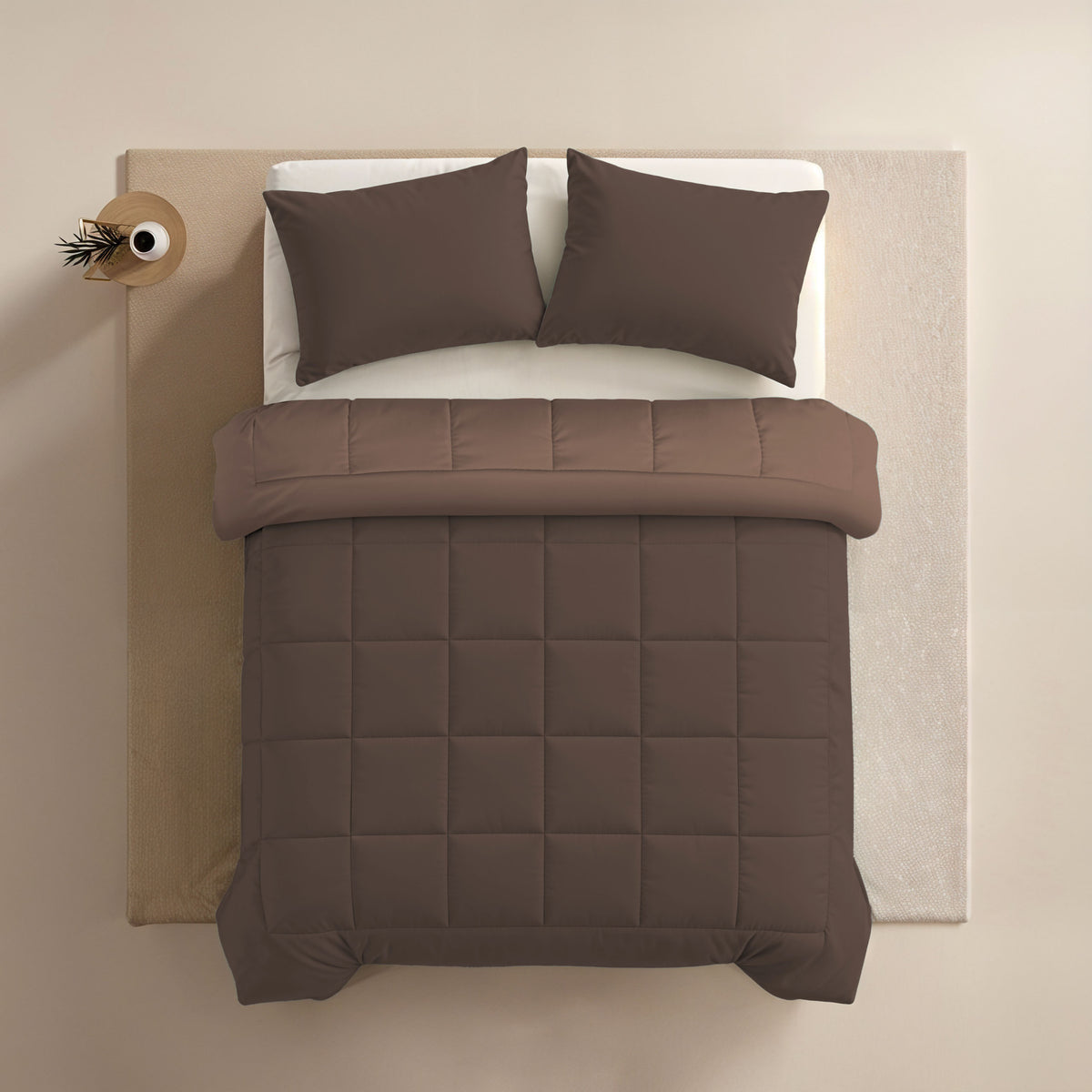 Bovenaanzicht van een netjes opgemaakt bed met het Zelesta Comfort Duo Dekbed in Chocolade bruin & Mokka, twee bijpassende kussens, fris witte lakens en een klein bijzettafeltje met een vaas.