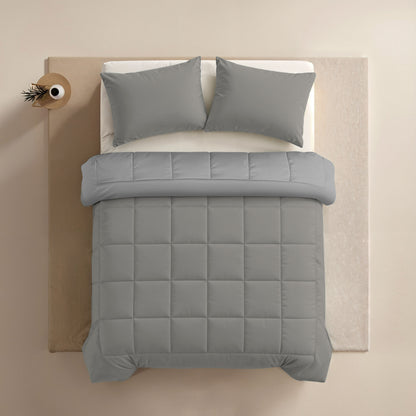 Een keurig opgemaakt bed met het Zelesta Comfort Duo Dekbed in Grijs & Zacht grijs en twee bijpassende kussens, van boven gefotografeerd op een licht vloerkleed met links een klein rond nachtkastje.