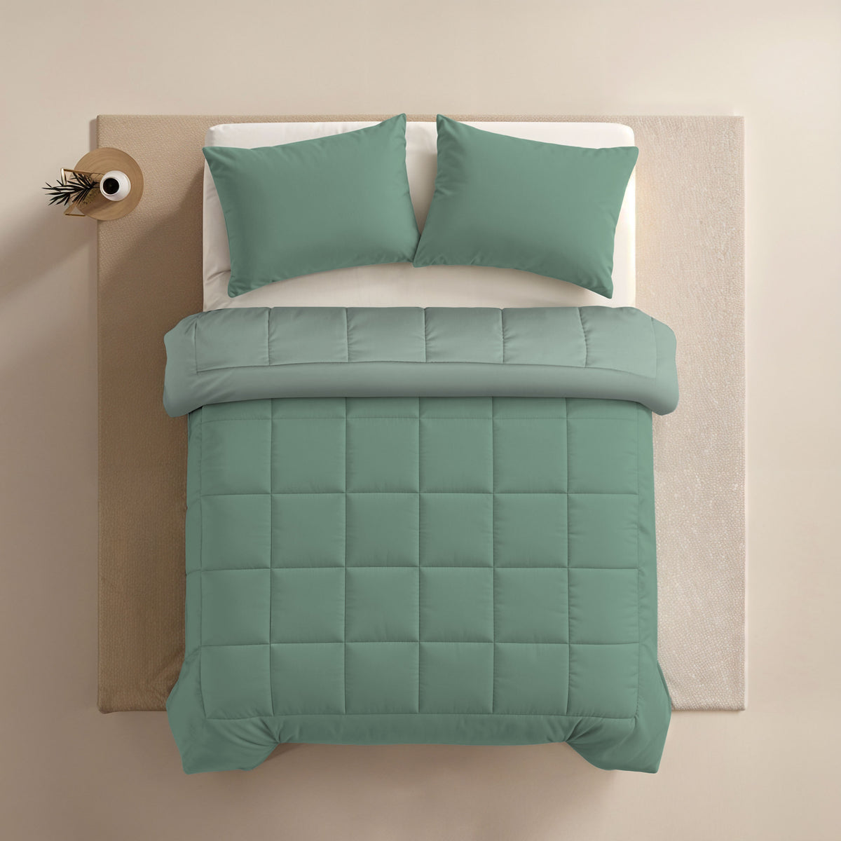 Een netjes opgemaakt bed met Zelesta Comfort Duo Dekbed in mint en lichtgroen, plus bijpassende groene kussens, van bovenaf gezien naast een kleine ronde tafel met een plant.