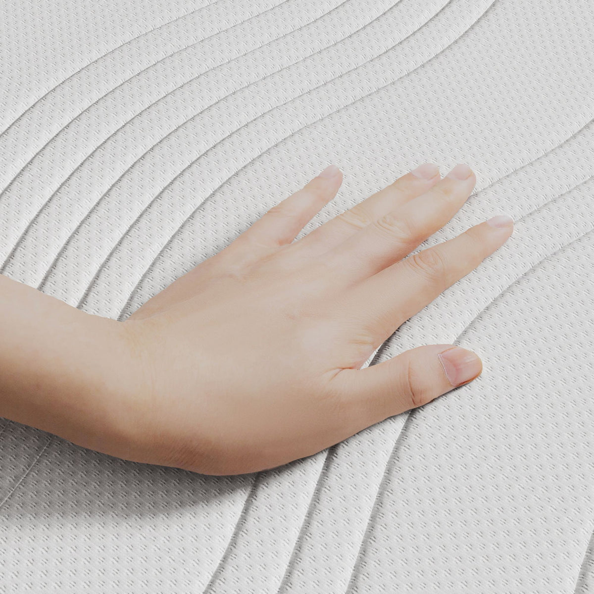 Een hand drukt op het gestructureerde, witte Topdekmatras - Comfortschuim Aloë Vera Tijk oppervlak met gebogen, verhoogde lijnen - ideaal voor een huisstofmijtwerend matrasgevoel.