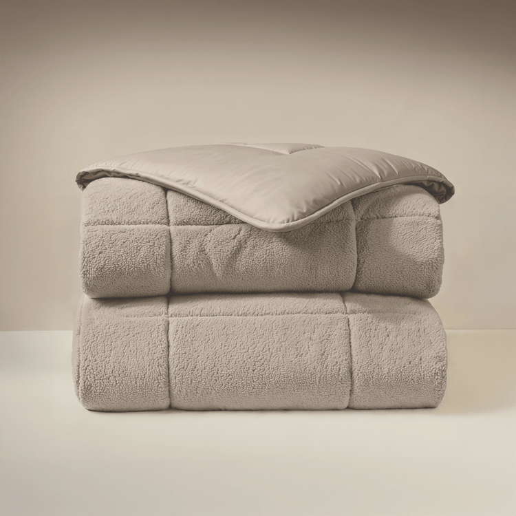 Het Zelesta Teddybed - Taupe, met een zachte teddystoftextuur, is netjes gevouwen en gestapeld tegen een neutrale achtergrond.