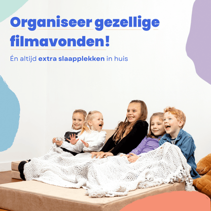 Vier kinderen zitten en liggen op de BAAAP speelbank in Emerald Green, onder een deken, lachend en blij. Ontdek urenlang speelplezier én gezellige filmavonden thuis met deze geliefde Nederlandse speelbank!.