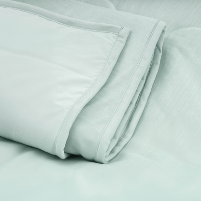 Een netjes opgevouwen mintgroene Zelesta Cooling Blanket rust op een oppervlak van bijpassende stof en biedt een hypoallergene optie voor rustgevend, verfrissend comfort.