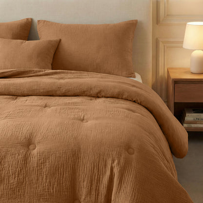 Een keurig opgemaakt bed met de Zelesta Japandibed Katoen Mousseline - Terra, twee kussens, een nachtkastje met een lamp en daaronder boeken opgestapeld.