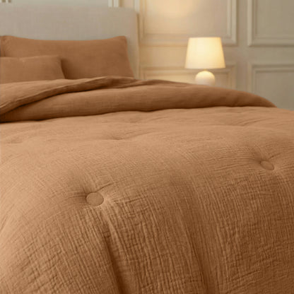 Een keurig opgemaakt bed met het Zelesta Japandibed Katoen Mousseline - Terra beddengoed staat bij een brandende lamp en een wand met panelen, waardoor een zacht verlichte Japandi slaapkamerambiance ontstaat.