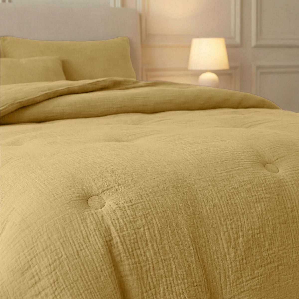 Een netjes opgemaakt bed met de Zelesta Japandibed Katoen Mousseline in Ochre met een bijpassend kussen en een brandende lamp op het nachtkastje in een zacht verlichte slaapkamer.