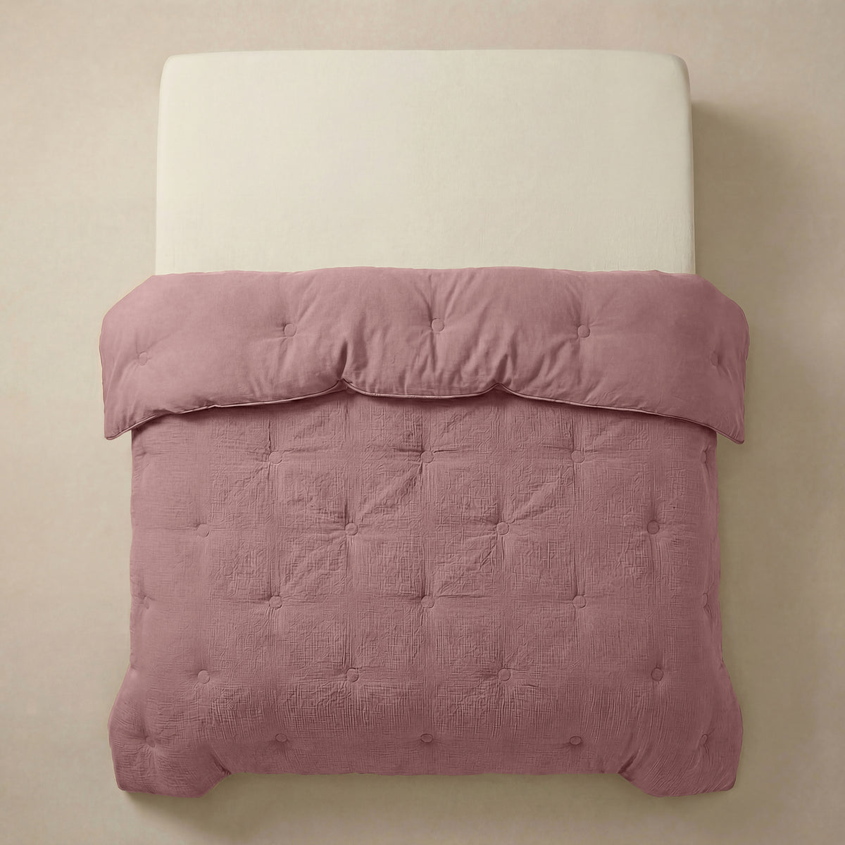 Een netjes opgemaakt bed met een crèmekleurig hoofdeinde en de Zelesta Japandibed Katoen Mousseline in Oudroze, getuft en zacht, tegen een neutrale muur.