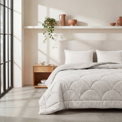 Een moderne slaapkamer met een netjes opgemaakt bed met het Zelesta Flanel Luxe - Creme microvezel dekbed, twee kussens, een houten nachtkastje en decoratieve items op een plank tegen een lichtgekleurde muur.