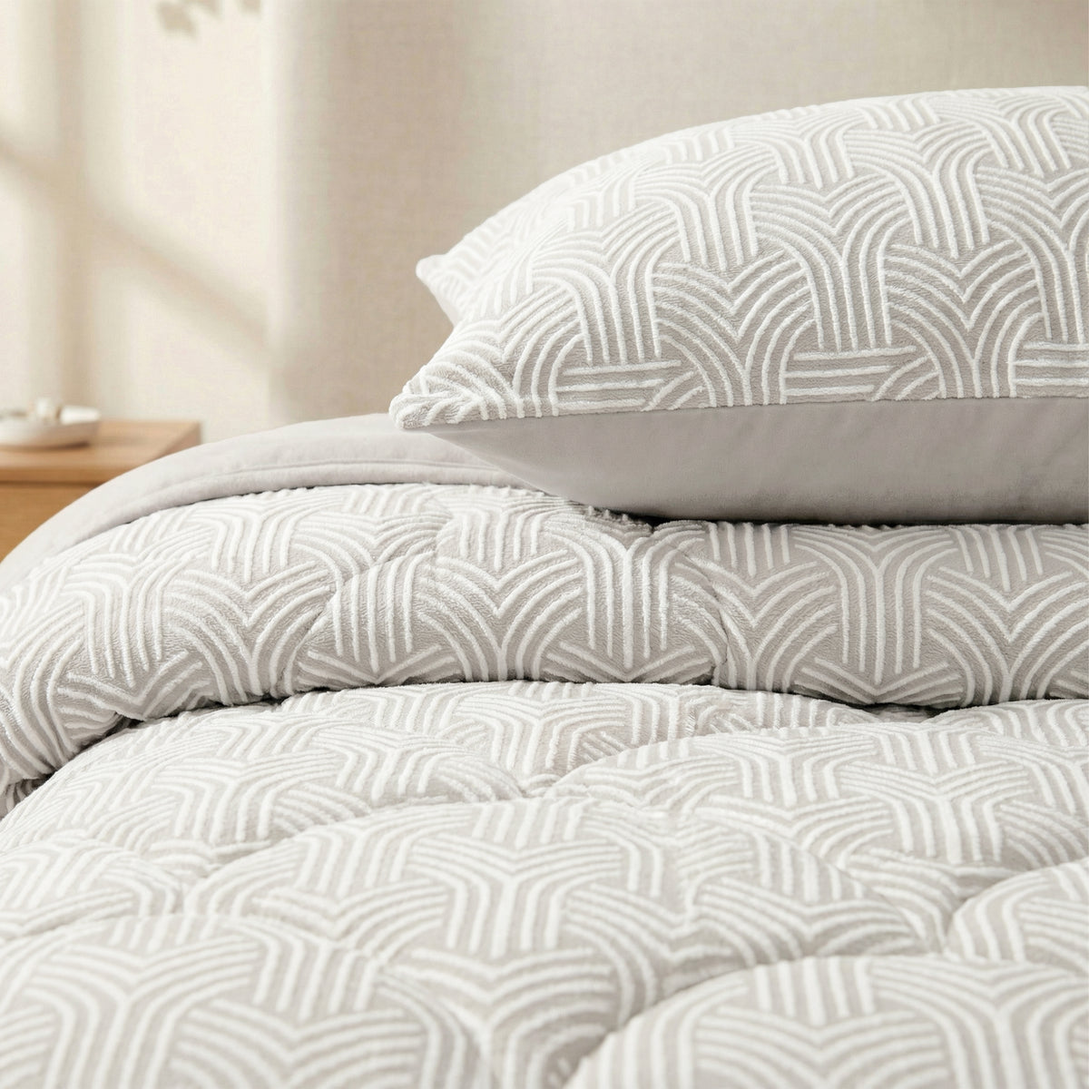 Close-up van een bed met het Zelesta Flanel Luxe - Creme dekbed en bijpassend kussen in lichtgrijze en witte geometrische patronen. Een klein nachtkastje verschijnt op de achtergrond.