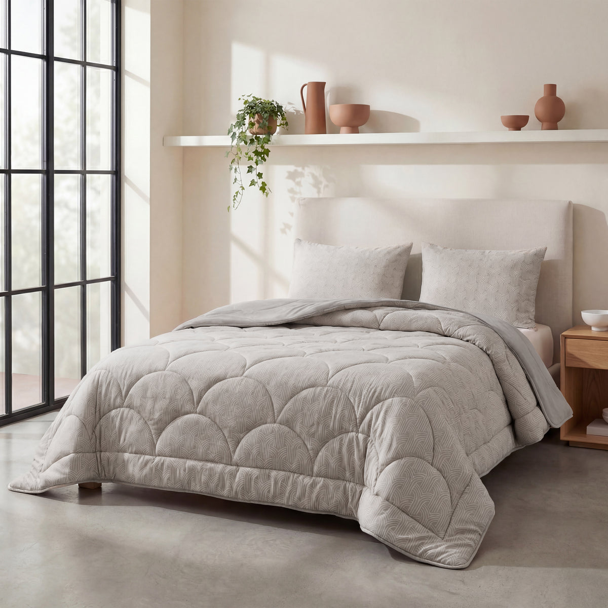 Een netjes opgemaakt bed met het Zelesta Flanel Luxe - Taupe & Grijs dekbed en twee kussens staat tegen een beige muur met een plank met decoratieve vazen en een potplant. Natuurlijk licht stroomt naar binnen door de grote ramen.