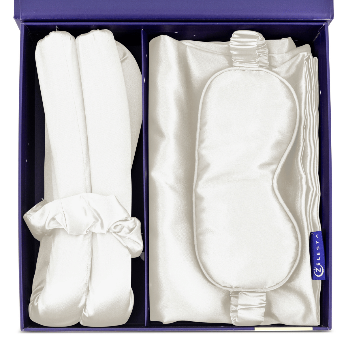 De Zelesta Sleeping Beauty Set - Pearl White bestaat uit een witte zijden slaapmasker, twee scrunchies en een gevouwen satijnen kussensloop, allemaal prachtig verpakt in een paarse geschenkdoos.