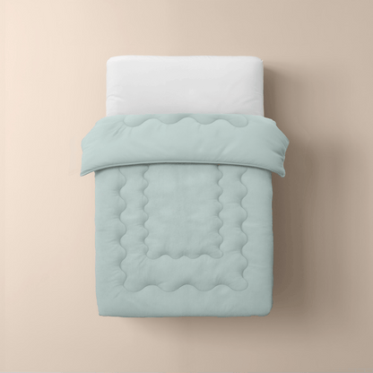 Een netjes opgemaakt eenpersoonsbed heeft een wit kussen en de mintgroene Zelesta Cooling Blanket, gewatteerd voor comfort, tegen een effen beige achtergrond voor een frisse en uitnodigende look.