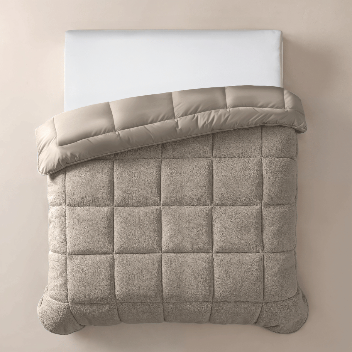 Een netjes opgemaakt bed met een wit kussen en het Zelesta Teddybed - Taupe, met een beige rasterpatroon, omgeslagen aan de bovenkant, gefotografeerd van bovenaf.