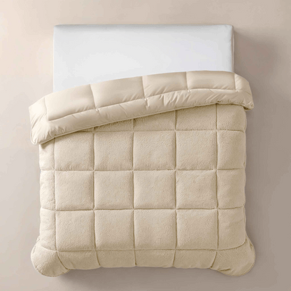 Het Zelesta Teddybed - Crème heeft een wit kussen en een crèmekleurig pluche teddystof dekbed met rasterpatroon dat is omgeslagen om de pluche textuur te laten zien, tegen een lichtbeige achtergrond.