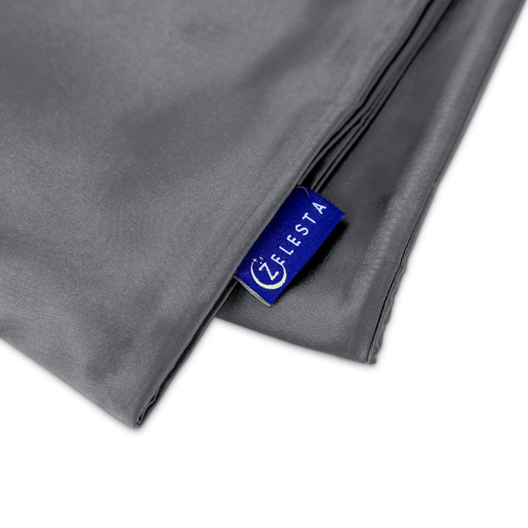 Close-up van gevouwen grijze stof met een blauw Zelesta label, perfect voor de luxe Zelesta Sleeping Beauty Set - Amazing Anthracite kussensloop of anti-aging slaapmasker.