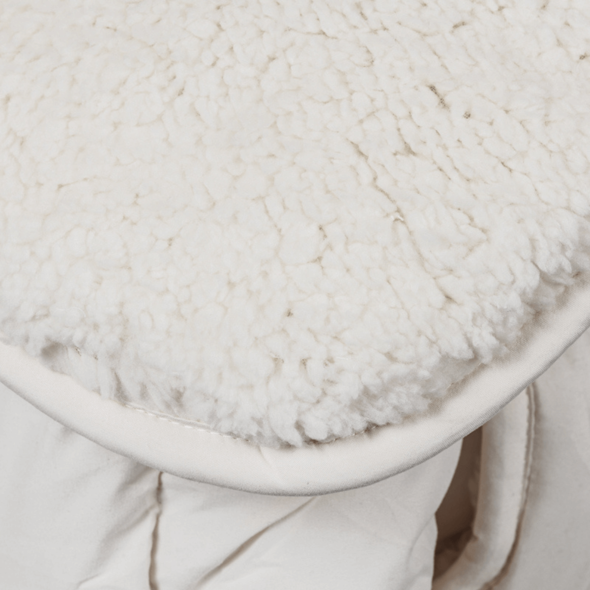 Close-up van zachte, witte pluche teddystof gedrapeerd over een lichtgekleurd gewatteerd dekbed, waarschijnlijk de Zelesta Teddybed - Crème deken, jas of beddengoed.