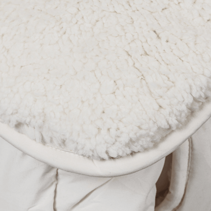 Close-up van zachte, witte pluche teddystof gedrapeerd over een lichtgekleurd gewatteerd dekbed, waarschijnlijk de Zelesta Teddybed - Crème deken, jas of beddengoed.