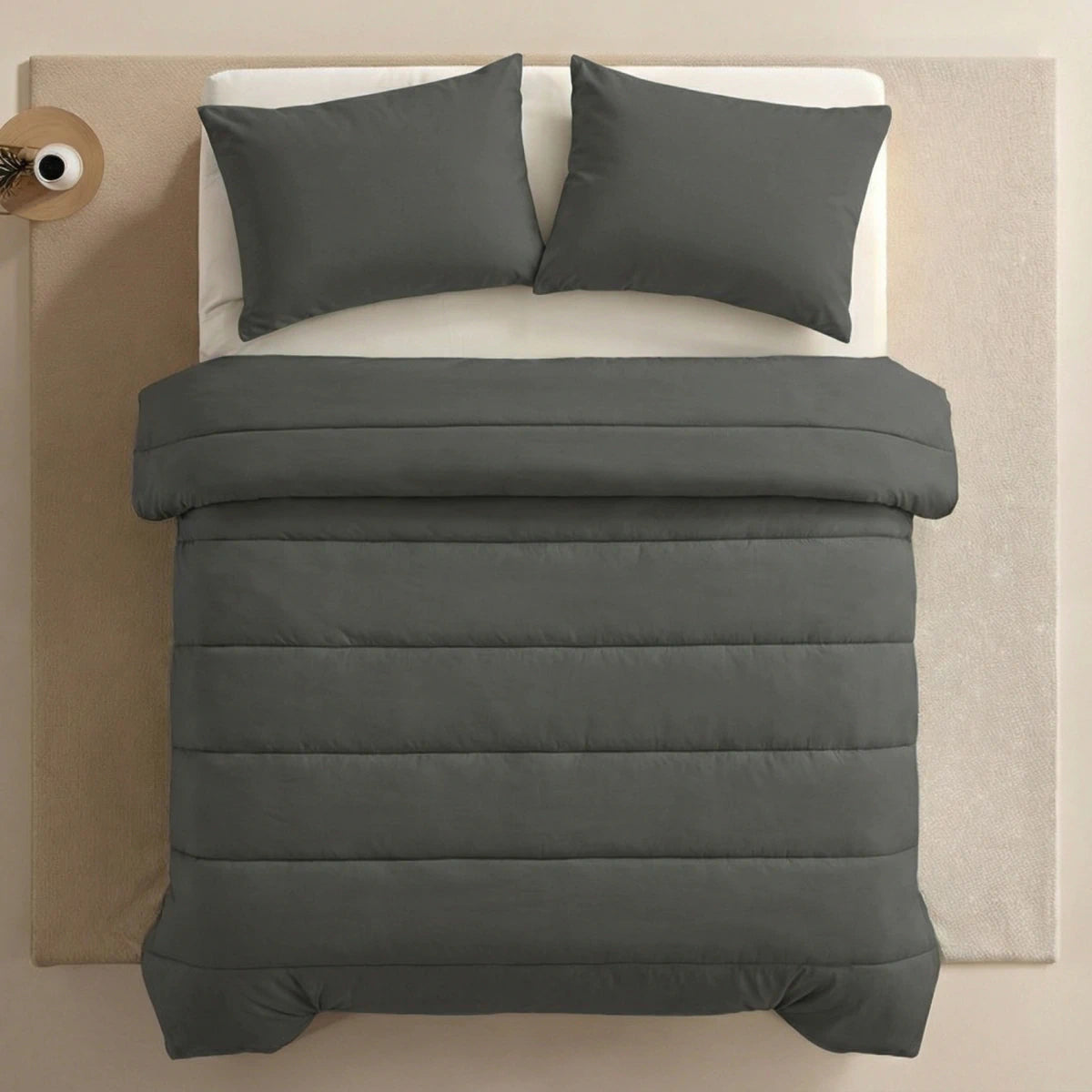 Een netjes opgemaakt bed met donkergrijs superzachte microvezel beddengoed en twee Zelesta Comfort Uni kussenslopen (antraciet, 60x70cm), van bovenaf gezien, op een lichte vloer met links een rond nachtkastje.