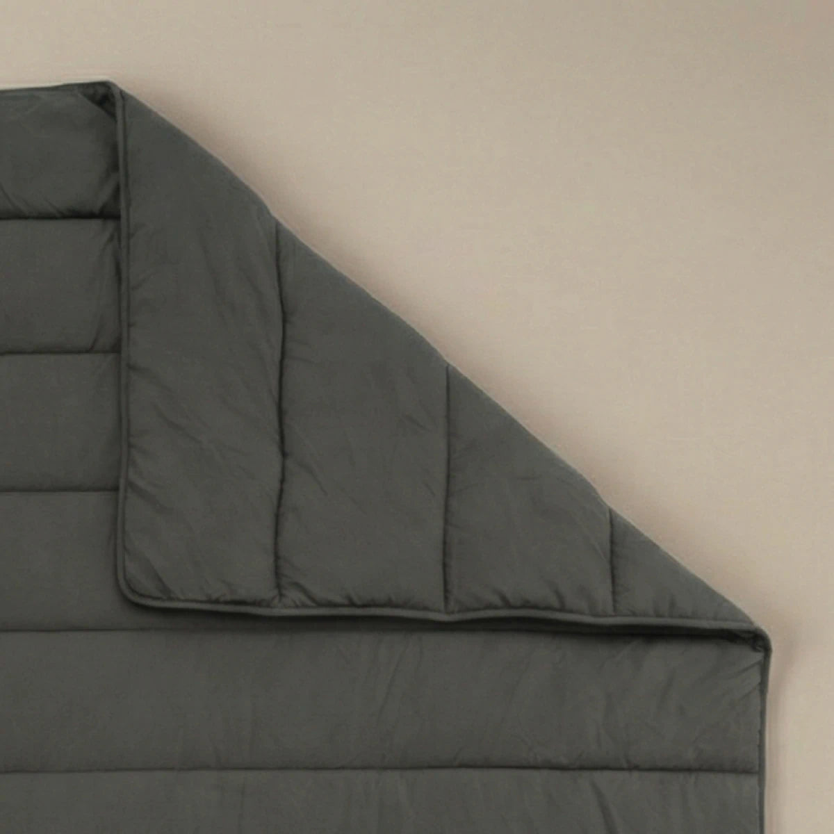 Het Zelesta Comfort Uni Dekbed in antraciet, met zijn donkergrijze doorgestikte ontwerp geïnspireerd op klassieke dekbedden, wordt plat op een neutrale ondergrond getoond, met één hoek omgevouwen om het stiksel en de dikte te onthullen.