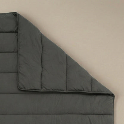 Het Zelesta Comfort Uni Dekbed in antraciet, met zijn donkergrijze doorgestikte ontwerp geïnspireerd op klassieke dekbedden, wordt plat op een neutrale ondergrond getoond, met één hoek omgevouwen om het stiksel en de dikte te onthullen.