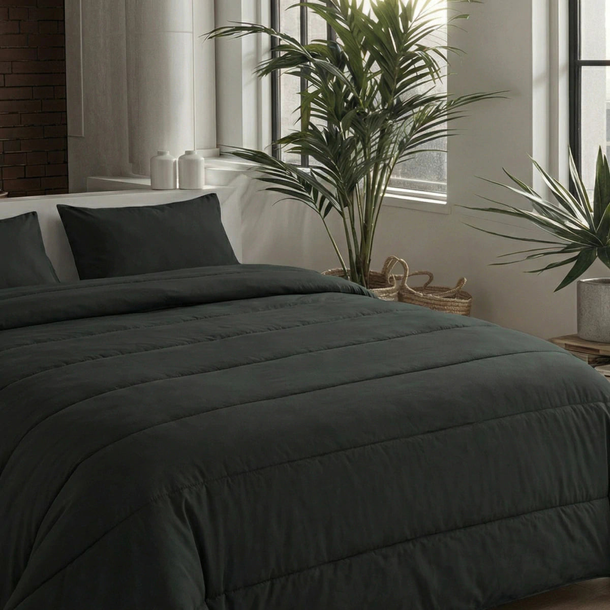 Een netjes opgemaakt bed met het Zelesta Comfort Uni Dekbed - Zwart en kussens staat bij grote ramen en groene potplanten in een moderne, minimale slaapkamer - ideaal voor comfort het hele jaar door.