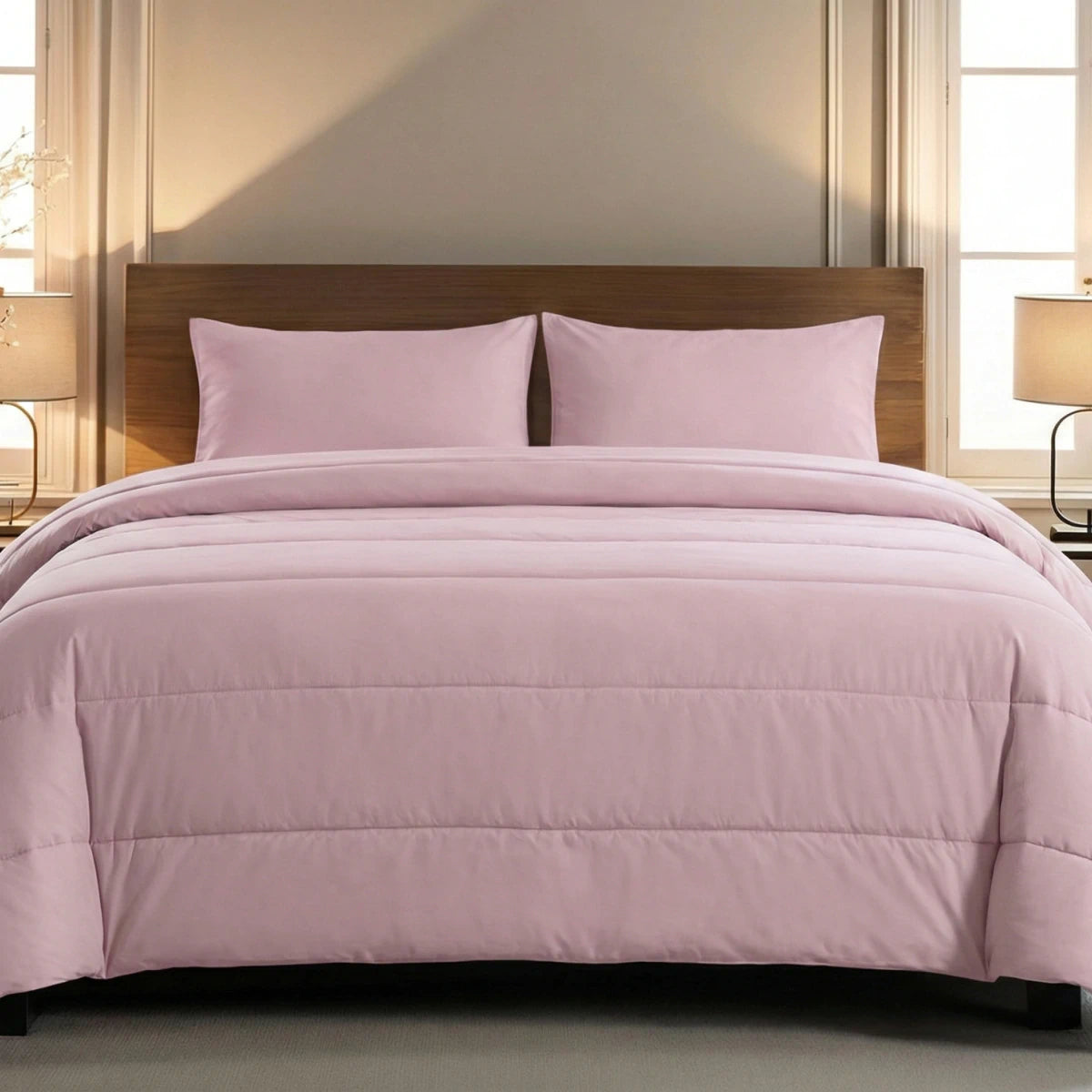 Een netjes opgemaakt bed met het Zelesta Comfort Uni Dekbed in Oud Roze en twee bijpassende kussens, tegen een houten hoofdeinde, biedt het hele jaar door comfort, met lampen op nachtkastjes aan weerszijden.