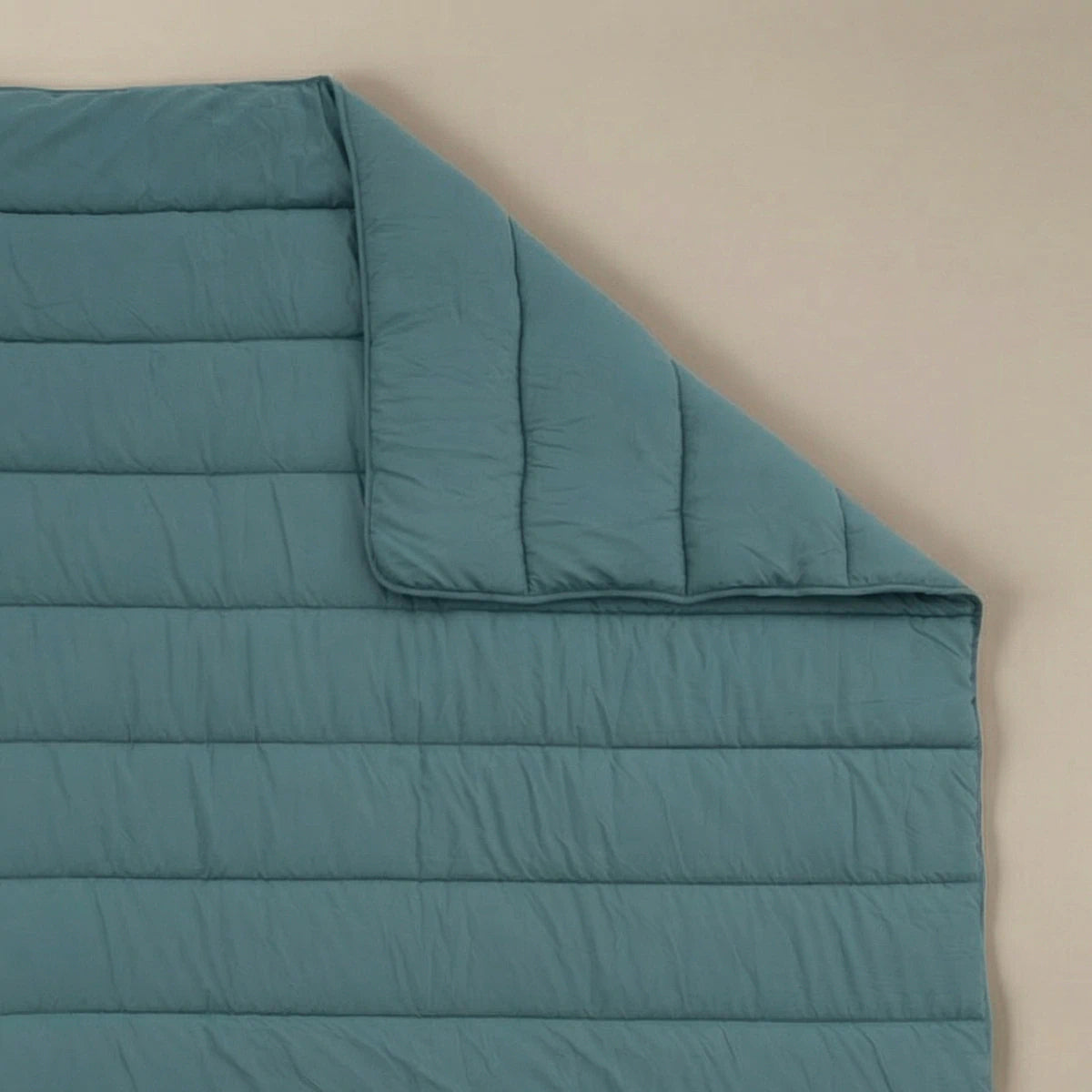 Het Zelesta Comfort Uni Dekbed in zeegroen, geïnspireerd op klassieke dekbedden, ligt plat op een beige oppervlak met een omgeslagen hoek - ideaal als laag voor elk seizoen in elke kamer.