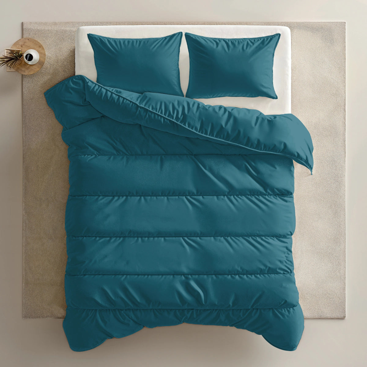 Een keurig opgemaakt bed met het Zelesta Everyday Uni Dekbed in Nachtblauw en twee bijpassende kussens, op een lichtgekleurd vloerkleed naast een kleine vaas op het nachtkastje.