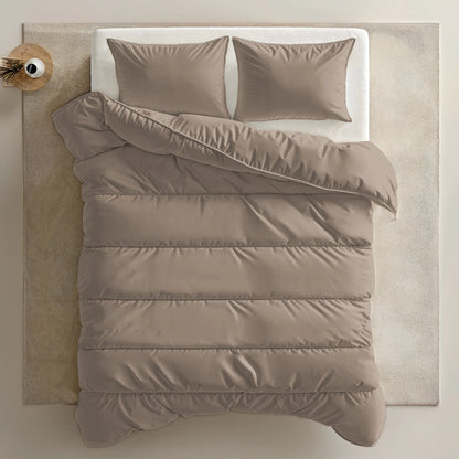 Een keurig opgemaakt bed met een Zelesta Everyday Uni Dekbed - Zachtbruin en twee kussens, op een lichtgekleurd vloerkleed naast een klein rond bijzettafeltje met een plant.
