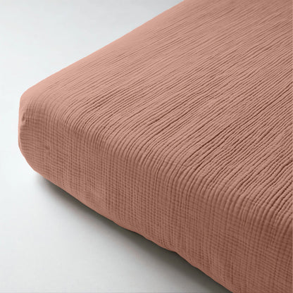Close-up van de Mousseline Hoeslaken - Dusty-Rose, een zachtroze hoeslaken van ademend geribd katoen dat een matrashoek bedekt - ideaal voor een serene Japandi-stijl.