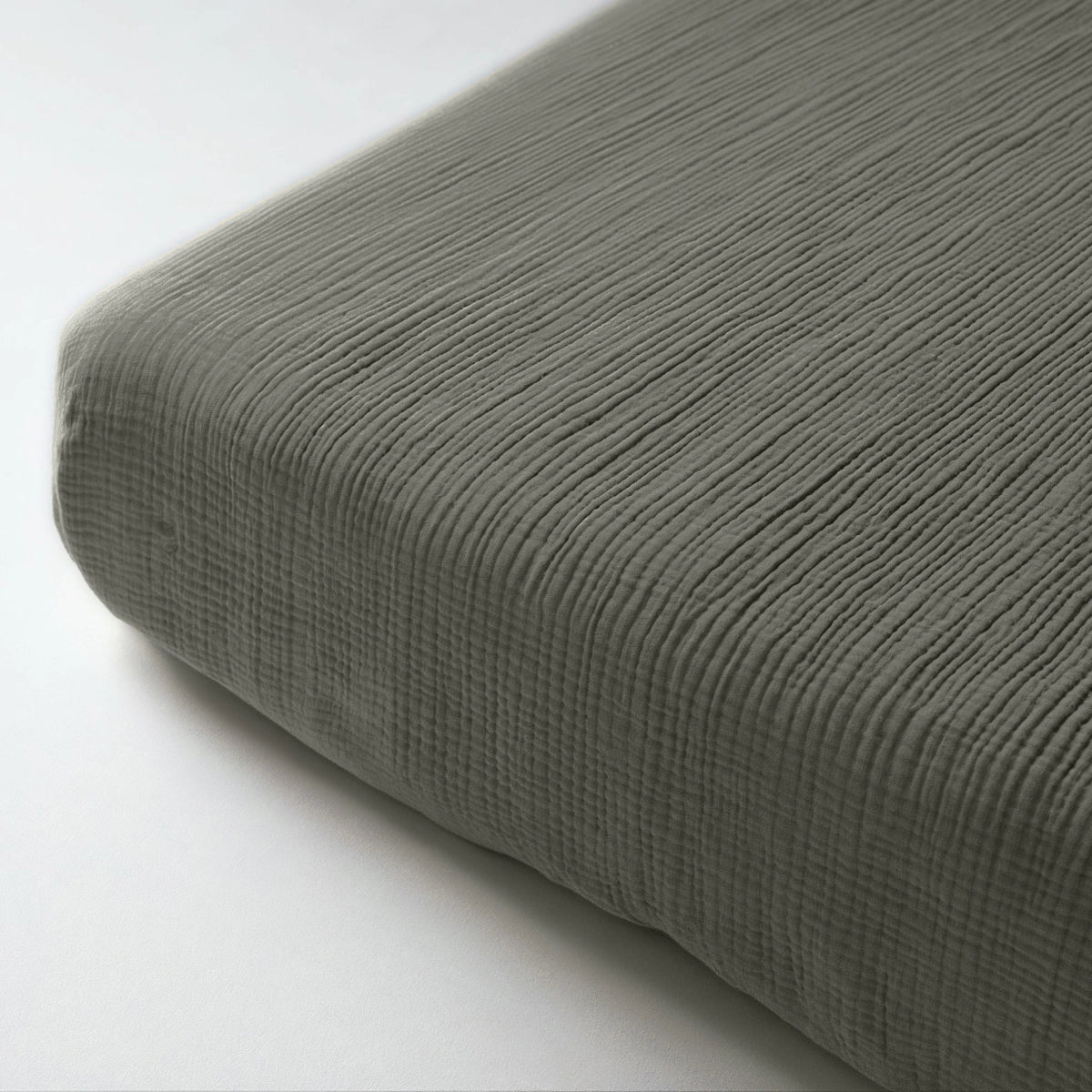 Close-up van het Mousseline Hoeslaken - Grijsgroen, gemaakt van ademend geribd mousseline katoen. Dit hoeslaken in Japandi-stijl combineert comfort en elegantie voor je matras.