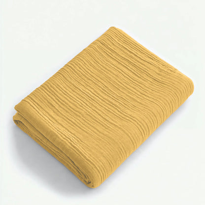Een Mousseline Hoeslaken in okergeel rust gevouwen op een wit oppervlak en laat de katoenstof met textuur zien - ideaal voor een adembenemende bedgoedlook.