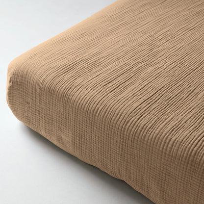Close-up van een hoek van de Mousseline Hoeslaken - Taupe met een geribbelde textuur op een matras gemaakt van zacht, ademend mousseline katoen voor comfortabel beddengoed in Japandi-stijl.