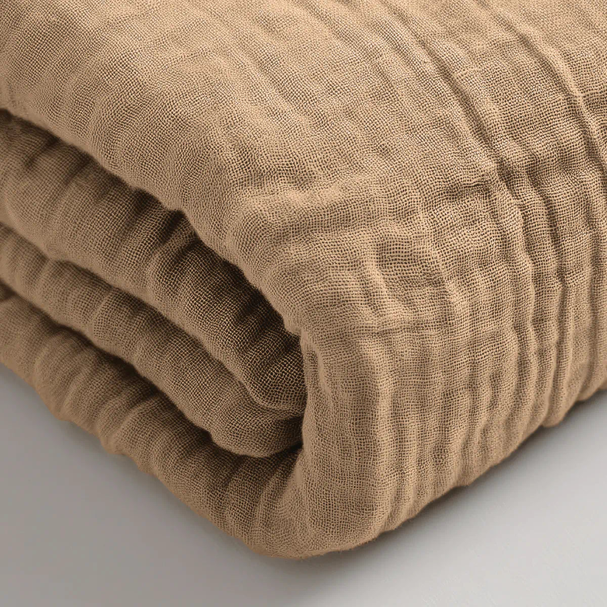 Een close-up van de Mousseline Hoeslaken in taupe, met een gestructureerde, lichtbruine katoenmix - ideaal voor wie op zoek is naar ademend beddengoed.