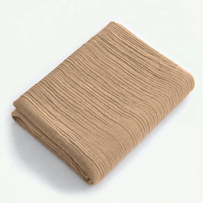 Een gevouwen taupe Mousseline Hoeslaken met een gestructureerd, gekreukt oppervlak op een effen witte ondergrond - ideaal voor fans van ademend beddengoed.