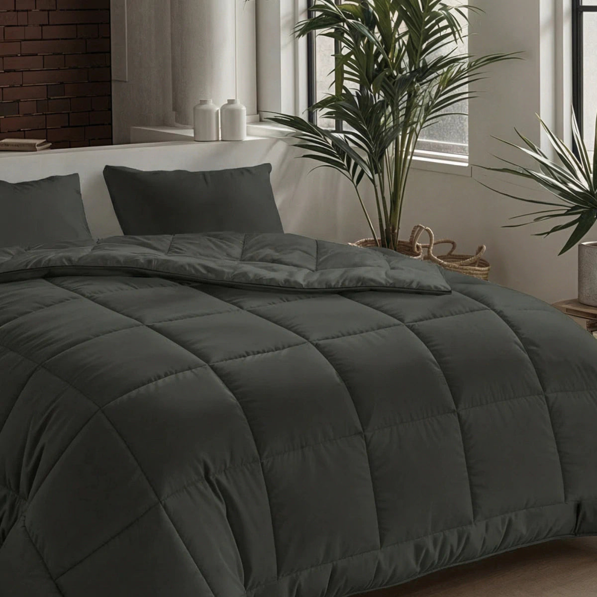 Een netjes opgemaakt bed met de Zelesta Pure Uni Dekbed Katoen in olijfzwart en kussens, in een moderne kamer met planten en natuurlijk licht, biedt een adembenemend slaapcomfort.
